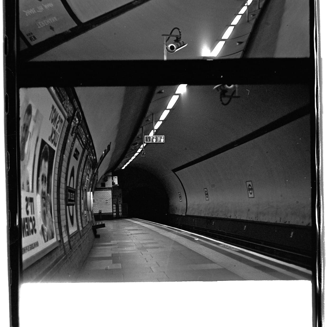 A digital scan of a black-and-white film negative of a deep-level London Underground station.